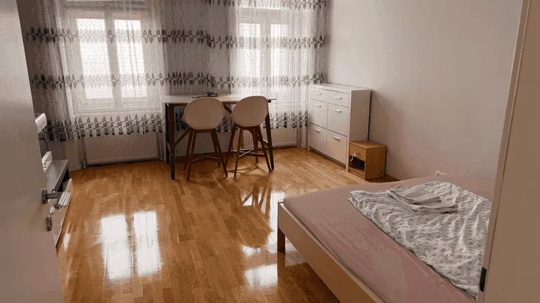 Helles Schlafzimmer mit Holzboden, einem Bett und einem kleinen Arbeitsbereich am Fenster.