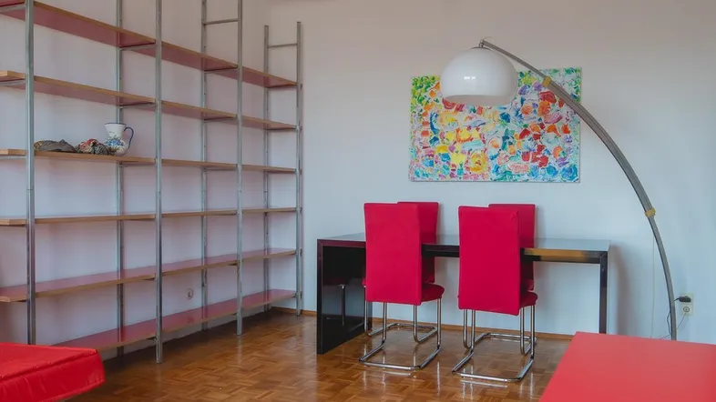 Heller Wohn- und Essbereich mit Parkettboden, großem Regal und farbenfroher Kunst.