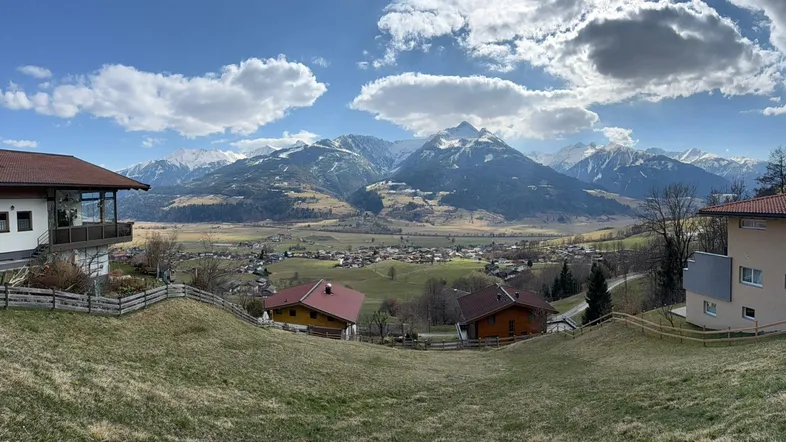 Weitläufiger Panoramablick über ein Tal mit Häusern, grünen Feldern und schneebedeckten Bergen.
