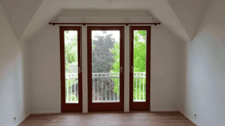Heller Raum im Dachgeschoss mit Laminatboden und drei französischen Balkontüren mit Blick ins Grüne.