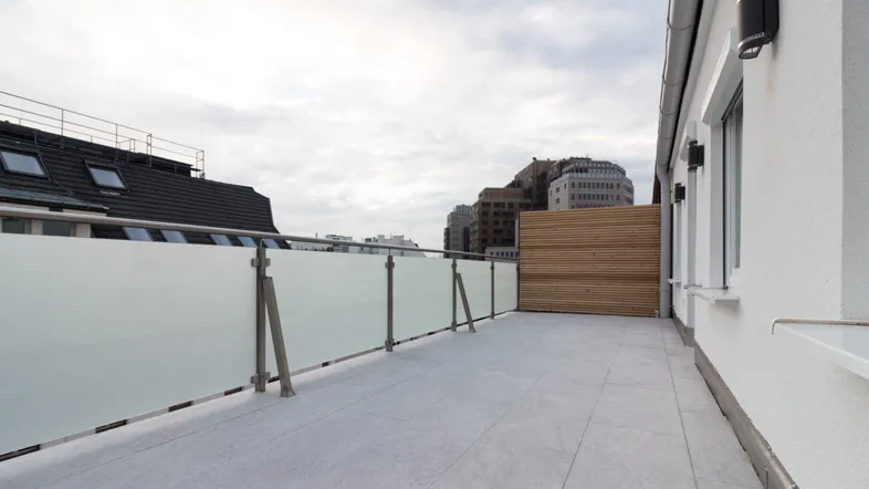 Geräumige Dachterrasse mit modernen Fliesen, Glasgeländer und Holzelementen unter bewölktem Himmel.