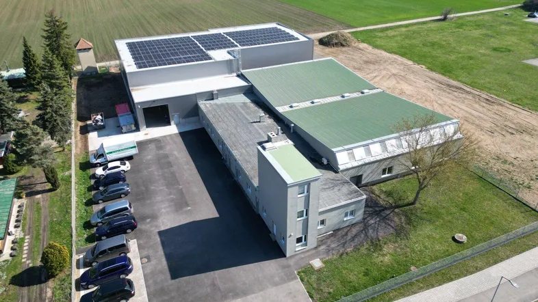 Luftaufnahme eines modernen Industriegebäudes mit Solaranlage und Parkplätzen, umgeben von Feldern.