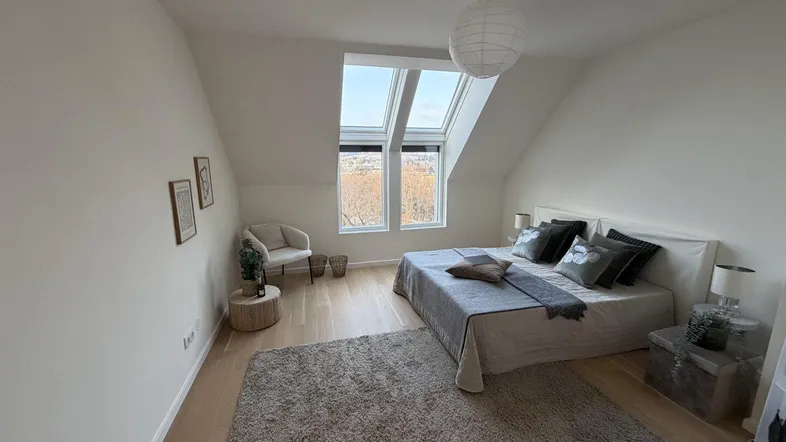 Helles Schlafzimmer im Dachgeschoss mit Holzboden, großem Bett und schrägen Dachfenstern.