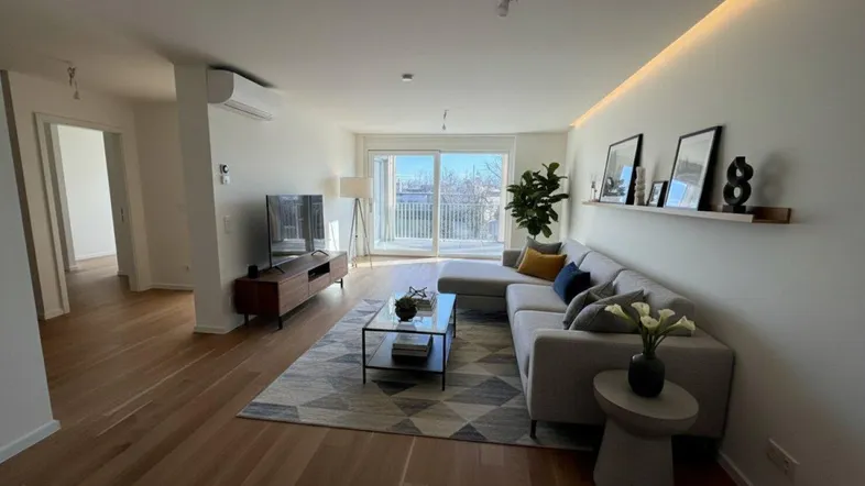 Helles Wohnzimmer mit modernem Sofa, Holzboden und Zugang zu einem Balkon mit Stadtblick.