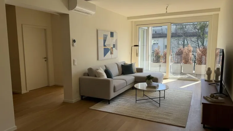 Helles Wohnzimmer mit modernem Sofa, Holzboden und Zugang zu einem sonnigen Balkon.