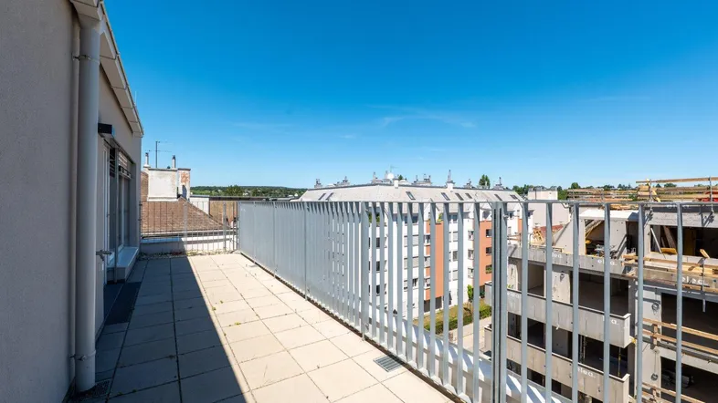 Geräumige Dachterrasse mit Fliesenboden und Metallgeländer, bietet einen weiten Blick über die Stadt.