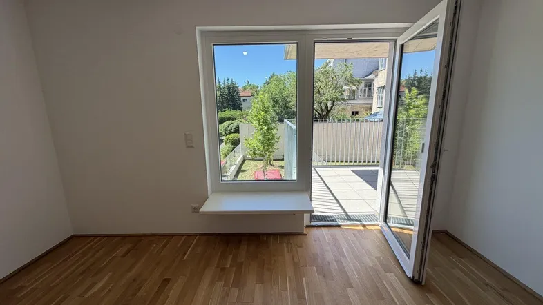 Helles Zimmer mit Parkettboden und direktem Zugang zu einem kleinen Balkon oder einer Terrasse.