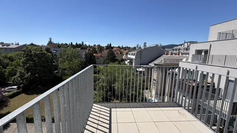 Geräumiger Balkon mit Fliesenboden und weitem Blick über die umliegende Wohngegend und viel Grün.