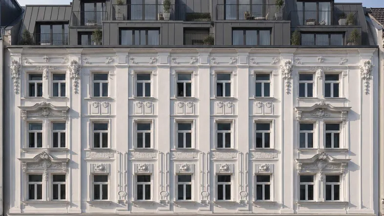 Weiße, reich verzierte Fassade eines Altbaus mit modernem Dachausbau und Balkonen.