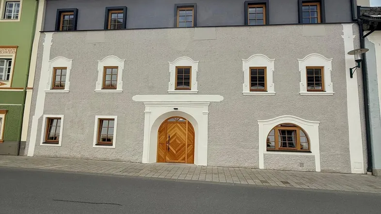 Historisches Gebäude mit renovierter Fassade und traditionellen Holzfenstern unter bewölktem Himmel.