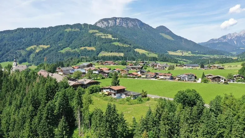 Panoramablick auf ein malerisches Dorf in den Bergen, umgeben von grünen Wäldern und Wiesen.
