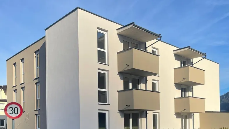 Modernes Mehrfamilienhaus mit klaren Linien und mehreren Balkonen unter blauem Himmel.
