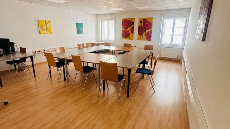Großer Konferenzraum mit U-förmiger Tischordnung, Holzfußboden und farbenfrohen Bildern an den Wänden.