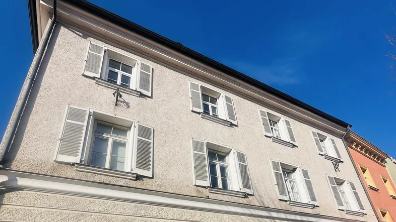 Fassade eines gepflegten Gebäudes mit vielen Fenstern und geöffneten Fensterläden unter blauem Himmel.