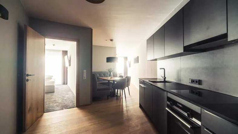Moderne Küche mit dunklen Schränken und Holzboden, offen zum Essbereich und Schlafzimmer.