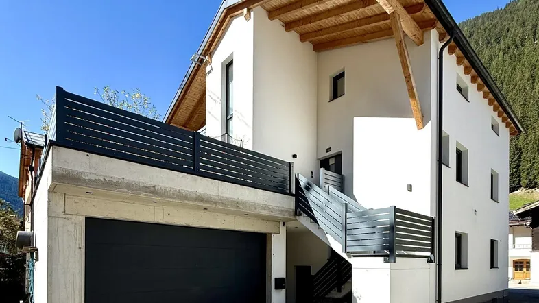 Modernes Wohnhaus mit weißer Fassade, Holzdetails und integrierter Garage in alpiner Umgebung.
