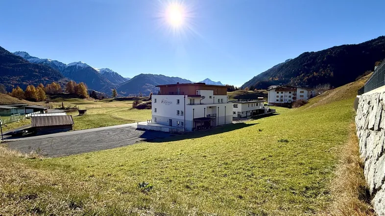 Modernes Gebäude in alpiner Landschaft mit sonnigem Bergblick und grünen Wiesen.