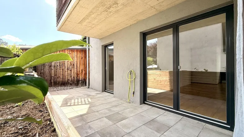 Große gepflasterte Terrasse mit Schiebetüren zum Innenbereich und Holzzaun im Hintergrund.