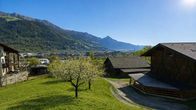Weitläufige Landschaft mit grünen Hügeln, alten Gebäuden und einem Panoramablick auf die Berge.