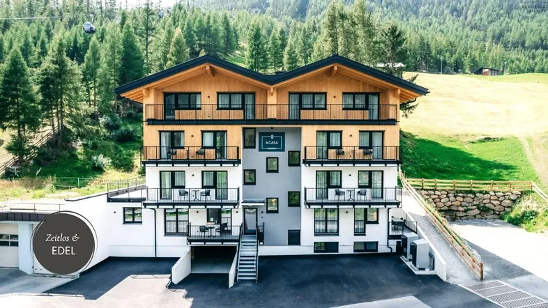 Modernes Apartmenthaus in den Bergen mit Holzelementen und Balkonen, umgeben von grüner Natur.
