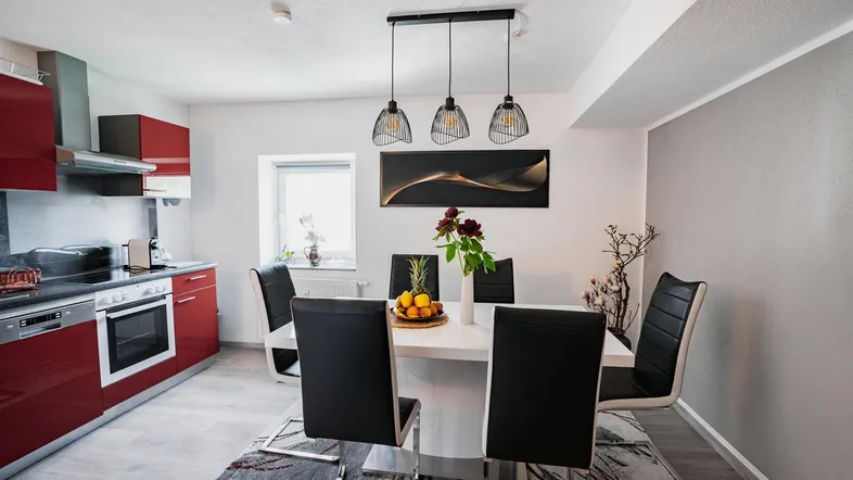 Moderne offene Küche mit Essbereich, roten Hochglanzfronten und stilvollen Pendelleuchten.