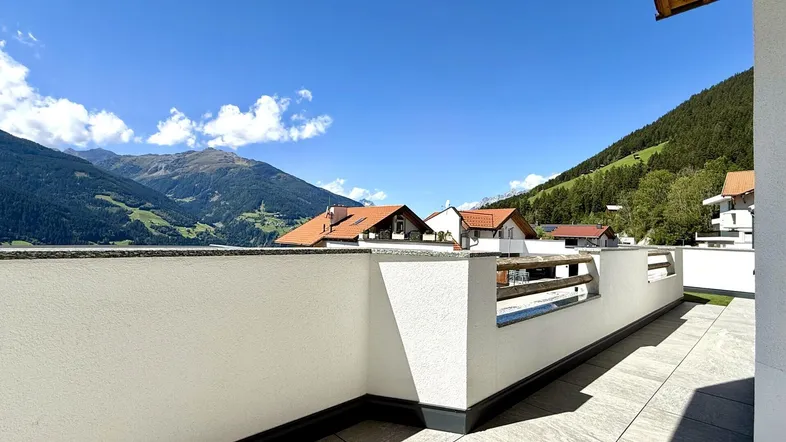Geräumige Terrasse mit Fliesenboden und beeindruckendem Bergblick unter blauem Himmel.