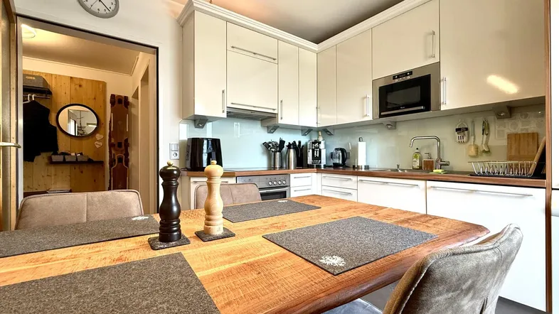 Moderne Küche mit weißen Schränken, Holztisch und Blick in den Flur.