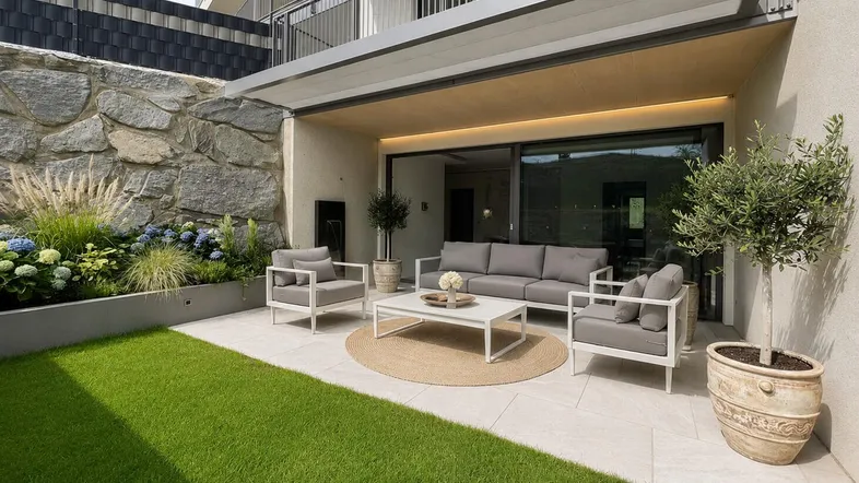 Moderne Terrasse mit bequemen Gartenmöbeln, Rasenfläche und Steinmauer, ideal zum Entspannen im Freien.