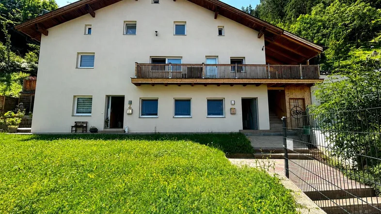 Traditionelles Haus mit Balkon und gepflegtem Vorgarten in sonniger Hanglage.