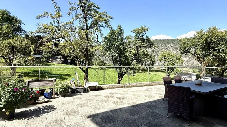 Geräumige Terrasse mit Gartenmöbeln, Blick ins Grüne und auf die umliegende Berglandschaft.