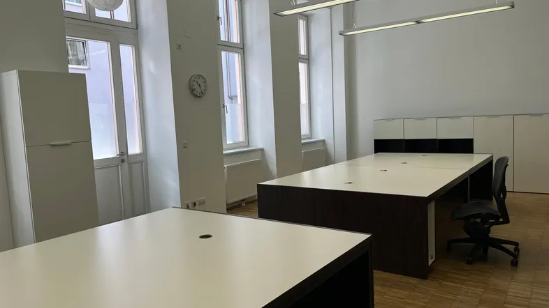 Geräumiges Büro mit mehreren Arbeitsplätzen, großen Fenstern und hellem Holzfußboden.
