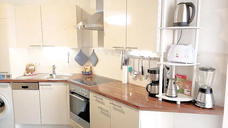Moderne Einbauküche mit hellen Fronten, Holztheke, Induktionskochfeld und diversen Elektrogeräten.