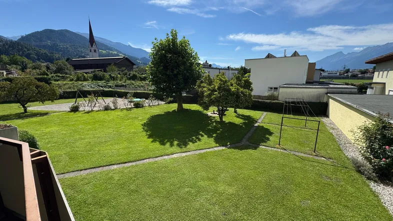 Großer Gemeinschaftsgarten mit Rasenfläche, Spielplatz und malerischem Bergblick im Hintergrund.