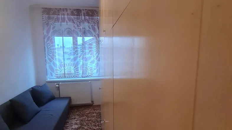 Kleines Wohnzimmer mit Sofa, Teppichboden und Fenster mit Vorhängen.