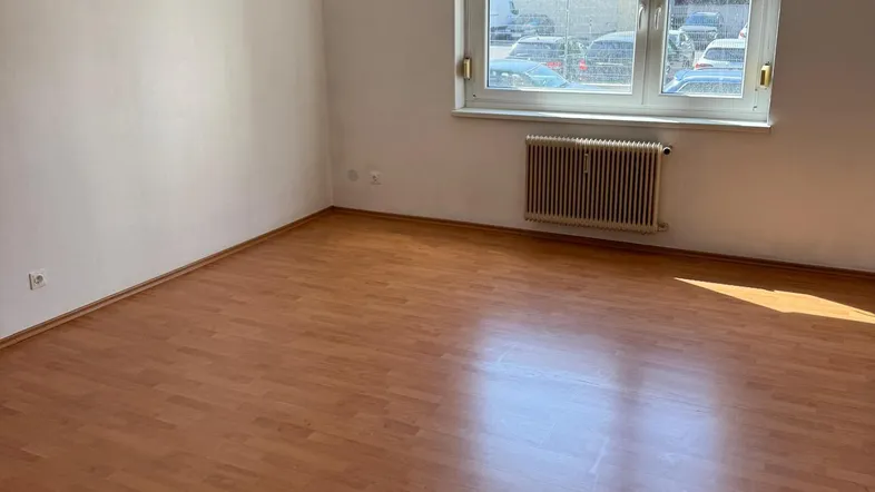 Helles Zimmer mit Holzboden und Blick auf die Straße, ausgestattet mit einem Heizkörper unter dem Fenster.