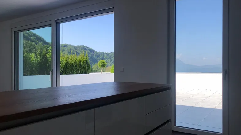Heller Raum mit Kücheninsel und großem Fenster mit Blick auf die Berge und die Terrasse.