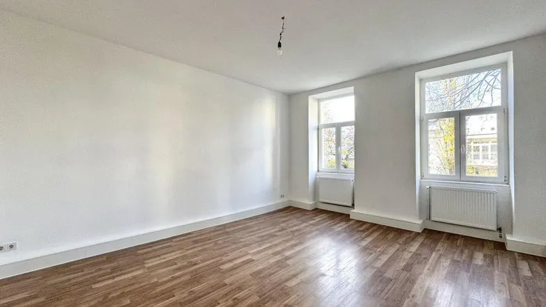 Helles Zimmer mit Holzboden und zwei Fenstern, bietet viel Tageslicht und Ausblick.