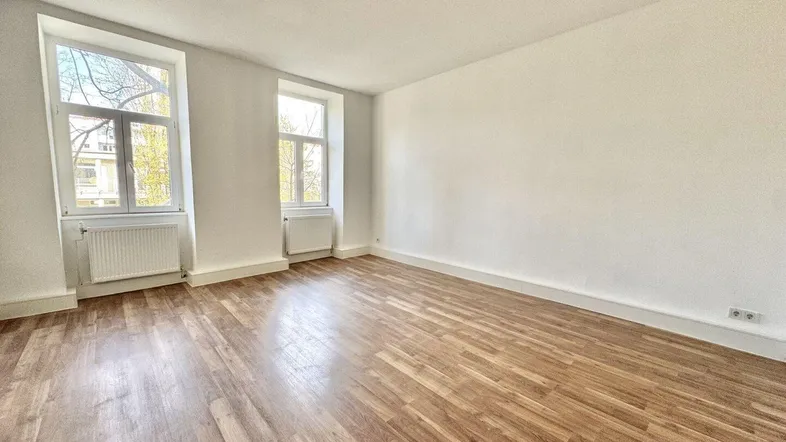 Helles Zimmer mit Holzboden und zwei Fenstern, bereit zur individuellen Gestaltung.