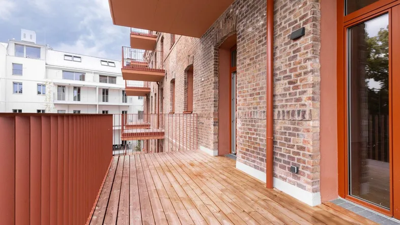 Geräumiger Balkon mit Holzfußboden und Blick auf die moderne Wohnanlage.