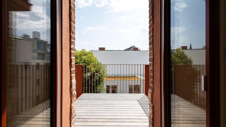Blick von einem Balkon mit Holzbelag und Metallgeländer auf den begrünten Innenhof.