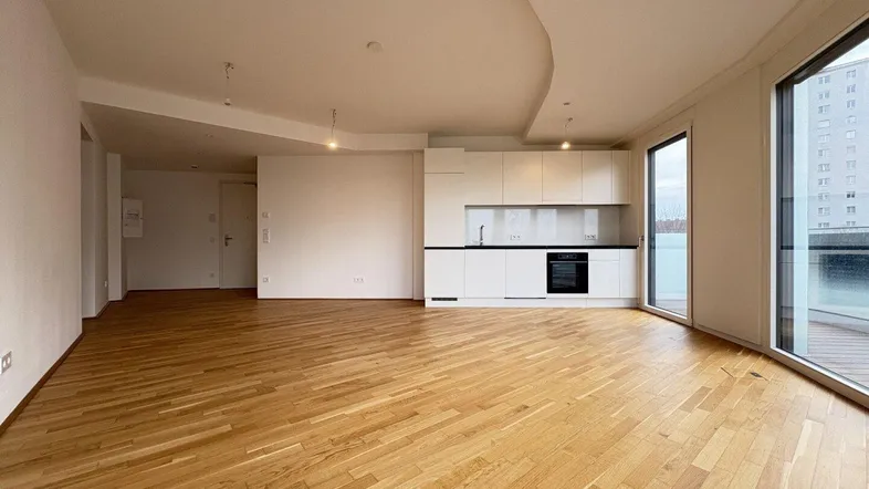 Heller, offener Wohnbereich mit integrierter Küche, Parkettboden und Zugang zu einem Balkon.