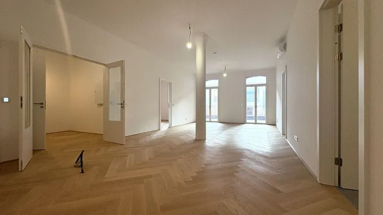 Geräumiger, heller Wohnbereich mit Fischgrätparkett und Zugang zu französischen Balkonen.