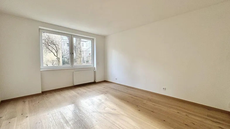 Helles, leeres Zimmer mit neuem Parkettboden und großen Fenstern, bereit zur individuellen Gestaltung.
