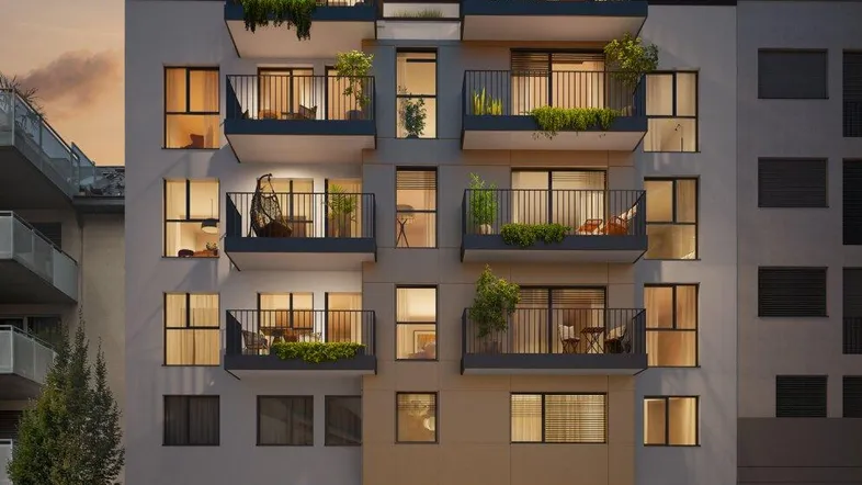 Moderne Wohnhausfassade mit Balkonen und beleuchteten Innenräumen bei Sonnenuntergang.
