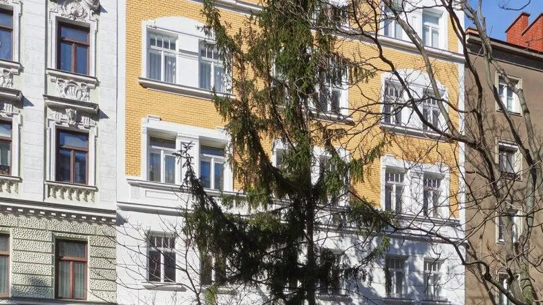 Fassade eines Mehrfamilienhauses mit gelben und weißen Putzflächen und hohen Fenstern.