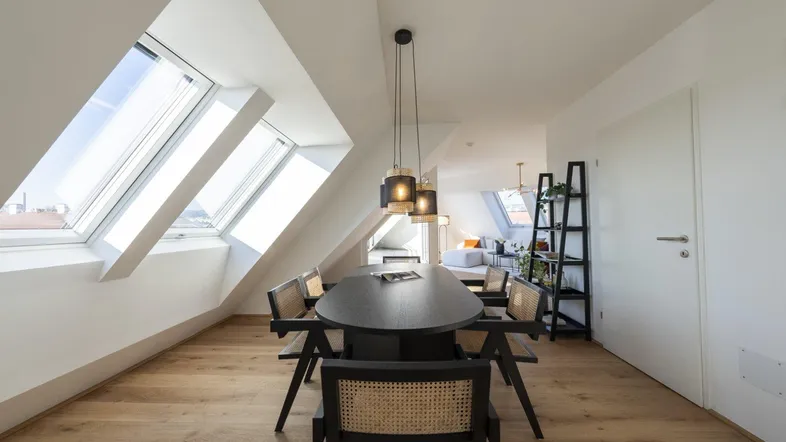 Heller Essbereich im Dachgeschoss mit Holzboden, modernen Möbeln und großen Dachfenstern.