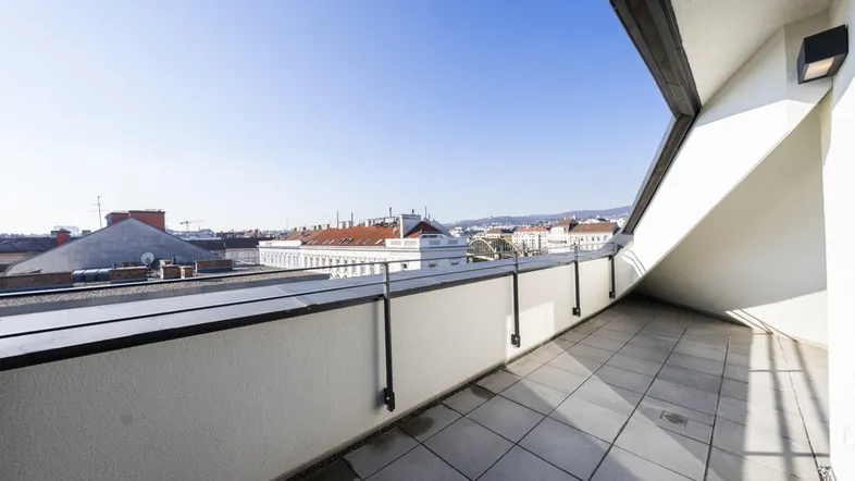 Geräumiger Balkon mit Fliesenboden und weitem Blick über die Stadt unter blauem Himmel.