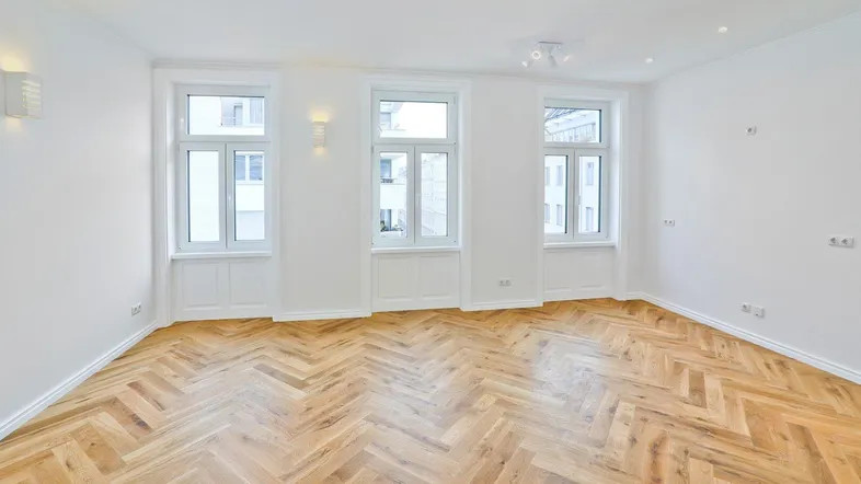 Heller Raum mit Fischgrätparkettboden und drei großen Fenstern, ideal als Wohnzimmer.