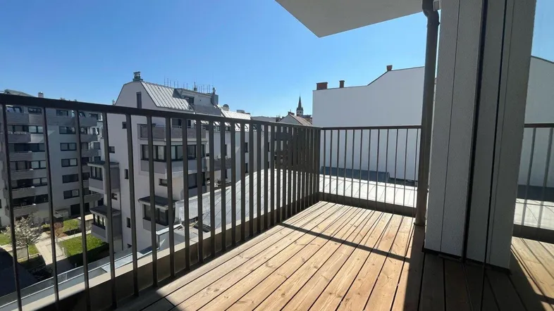 Geräumiger Balkon mit Holzboden und Blick auf die umliegenden Gebäude und den blauen Himmel.