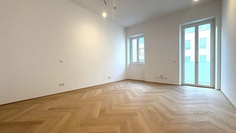 Helles Wohnzimmer mit Fischgrätparkett, weißen Wänden und Zugang zu einem Außenbereich.